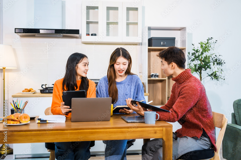 Three Asian young adult students sit around the kitchen table, attending online class on tablet. They engage in video conferencing, discussing lessons, taking notes, digital learning experience. Three Asian young adult students sit around the kitchen table, attending online class on tablet. They engage in video conferencing, discussing lessons, taking notes, digital learning experience.