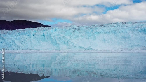 Panning camera movement view of the majestic Eqip Sermia glacier in Greenland, its towering wall of ice perfectly reflected in the calm waters of the Arctic Ocean. Greenland, Eqip Sermia