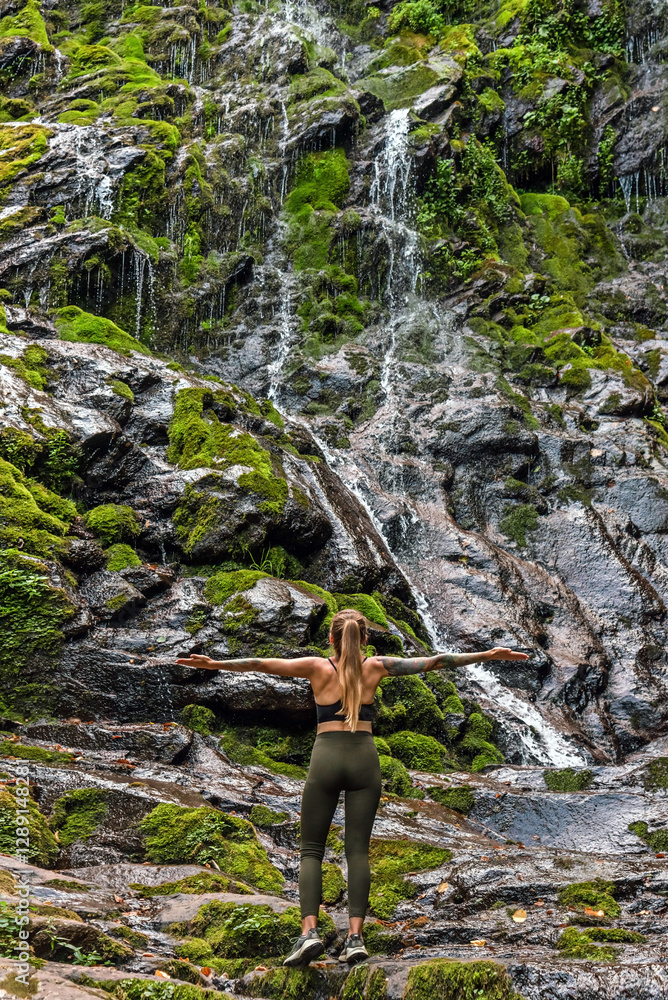 Woman Traveler Standing by Waterfall with Hands Outstretched