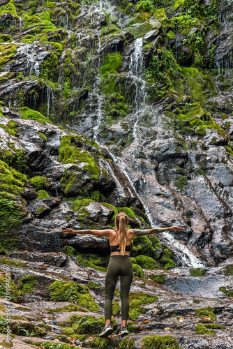 Woman Traveler Standing by Waterfall with Hands Outstretched photo