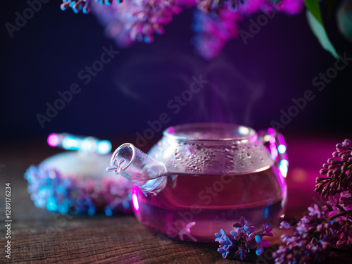 Lilac tea. Glass teapot on a wooden table with lilac petals