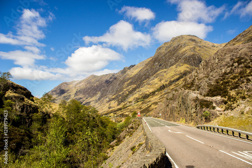 Bild auf Leinwand Road going through the Glen Coe Valley with the rugged Grampian Mountains rising