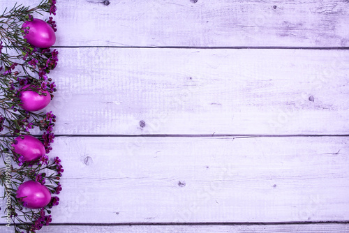 Easter composition with bright purple eggs and flowers on a light wooden background. Left-handed placement of elements creates empty space for text or design. photo