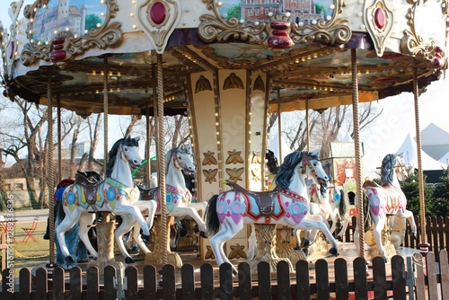 A beautifully decorated vintage carousel with ornate horses and glowing lights at an outdoor fair. The colorful details create a nostalgic and festive atmosphere