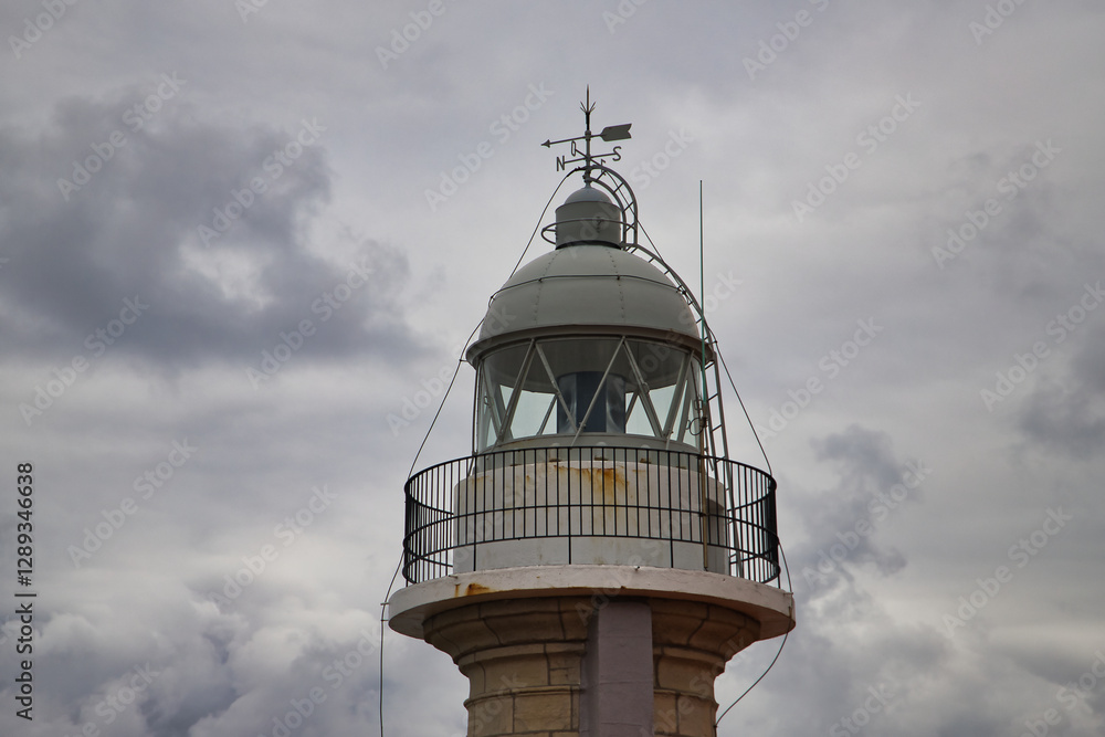 Detail of the top of the Torco lighthouse with its weather vane and lightning rod in the town of Suances in Cantabria, on a cloudy day at sunset. Concept travel, coast, cliffs, destinations, sea. Detail of the top of the Torco lighthouse with its weather vane and lightning rod in the town of Suances in Cantabria, on a cloudy day at sunset. Concept travel, coast, cliffs, destinations, sea.