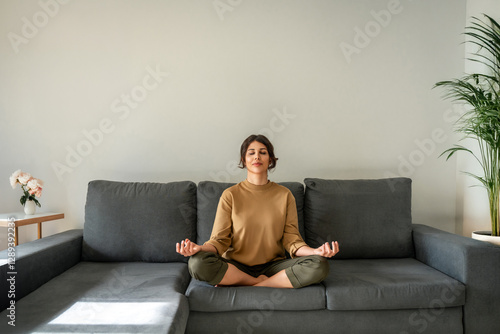 Konstfotografi Relaxed young indian woman sitting on couch, meditating with closed eyes in lotus pose