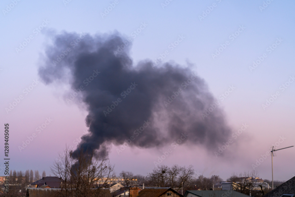 hick black smoke rising into the sky over residential buildings and trees at dusk. Environmental pollution and fire disaster concept. hick black smoke rising into the sky over residential buildings and trees at dusk. Environmental pollution and fire disaster concept.