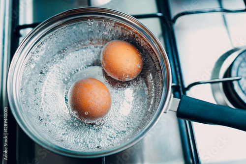Saucepan stainless steel with two boiling eggs breakfast in a water on a gas stove top view.