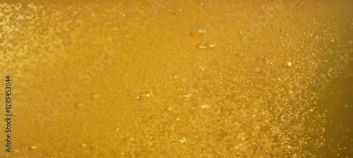 Golden beer pouring into glass with foam and many gas bubbles floating up in slow-motion. Close- up view