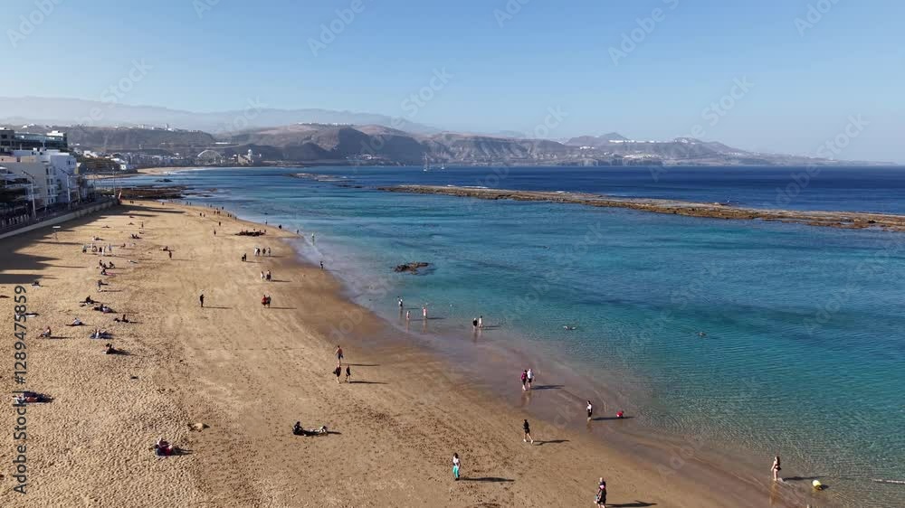 Exploring the beautiful coastline of Las Palmas de Gran Canaria on a sunny day with beachgoers enjoying the sand and sea Exploring the beautiful coastline of Las Palmas de Gran Canaria on a sunny day with beachgoers enjoying the sand and sea