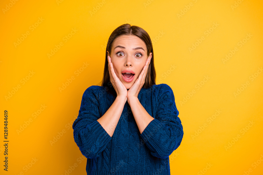 Photo of charming cheerful kind friendly girl having utterly been surprised by someone and rejoicing with hands touching cheeks while isolated over yellow background