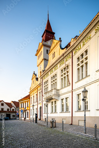 The historic Town Hall in Stara Boleslav stands proudly in the early morning light, showcasing its remarkable architecture along a quiet cobblestone street lined with trees.