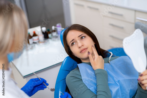 Patient has dental discomfort. A young woman at the dentist shows signs of discomfort while discussing her dental issues with the hygienist.