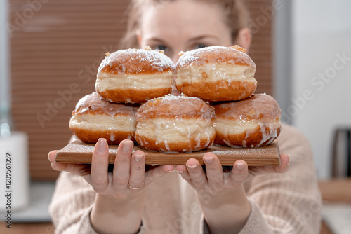 A cozy home setting with fresh Polish doughnuts (paczki) being sprinkled with powdered sugar. Soft, golden-brown pastries with icing and candied orange peel, perfect for Fat Thursday celebrations.