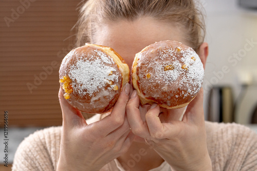 A woman holds a Polish paczek, a traditional Fat Thursday treat, filled with custard and glazed with sugar. A symbol of indulgence before Lent, paczki are deep-fried, fluffy, and sweet