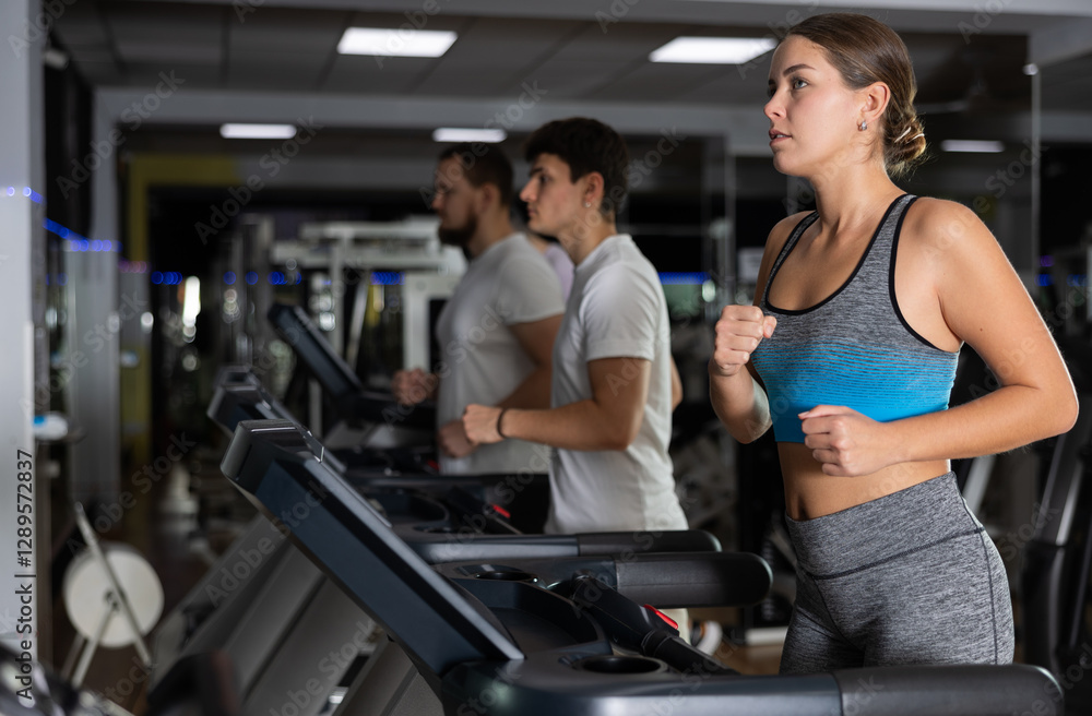 In gym, girl does exercises using treadmill. Young group of athletes trains in gym. Physical education and sports, active healthy lifestyle. In gym, girl does exercises using treadmill. Young group of athletes trains in gym. Physical education and sports, active healthy lifestyle.