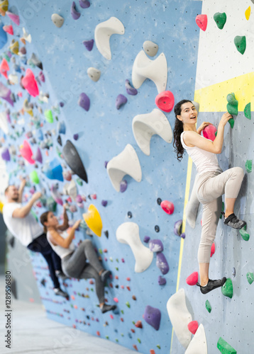 Motivated young girl climbing without ropes and harnesses on artificial bouldering wall in modern fitness center photo