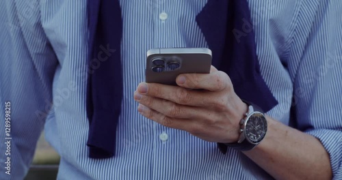 A businessman uses a mobile phone while standing in the city. Close-up of his hands