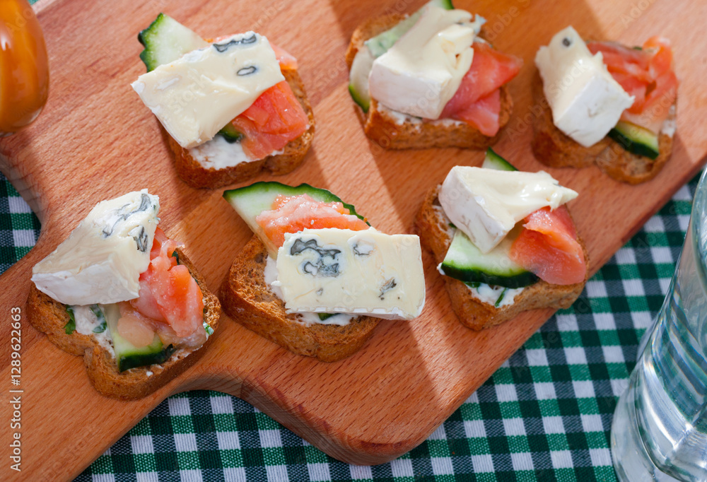 Canape with soft cheese at fresh bread with cucumber and salmon, served on wooden desk Canape with soft cheese at fresh bread with cucumber and salmon, served on wooden desk