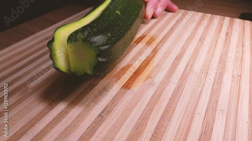 Chef slice zucchini with a closeview. Cutting long green courgettes in slow motion with a knife on a wooden board. Chopped courgette. Slow motion cooking video. Fresh italian salad with courgette. 
