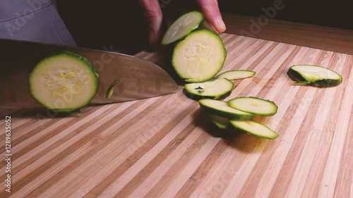 Chef slice zucchini with a closeview. Cutting long green courgettes in slow motion with a knife on a wooden board. Chopped courgette. Slow motion cooking video. Fresh italian salad with courgette. 