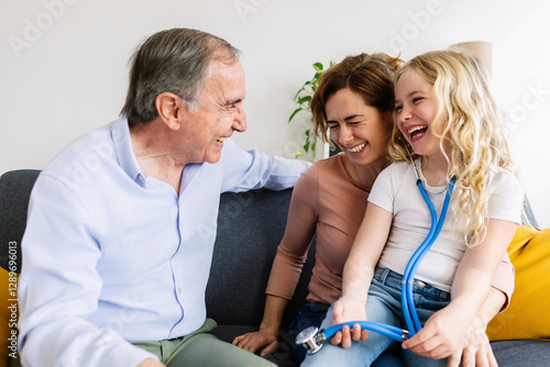 Εκτύπωση καμβά Little girl using a stethoscope, playing doctor with her family, everyone laughi