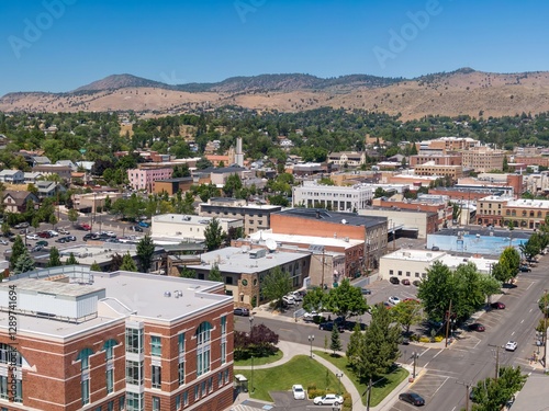 High-angle view of Klamath Falls town center, showcasing diverse architecture and ample parking. Sunny day, clear skies, and surrounding hills. Oregon, USA