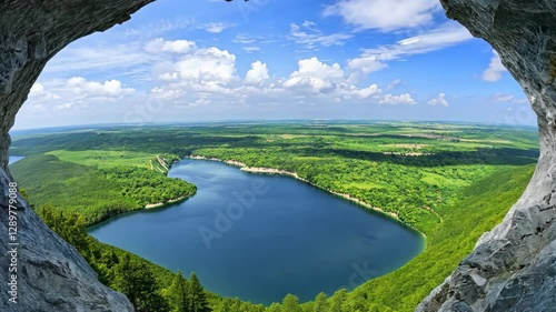 Breathtaking View of Winding River, Lush Green Forests, and Rolling Hills Through Natural Rock Arch Under Bright Blue Sky with Scattered Clouds, Creating Serene and Picturesque Nature Landscape
