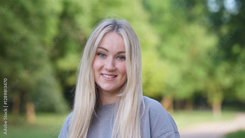 A cheerful young woman with long, flowing blonde hair beams with pure happiness in a vibrant park outdoors