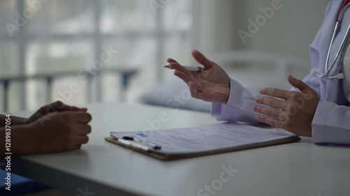 A doctor is talking to a patient in a hospital room. The patient is holding a pen and the doctor is holding a clipboard. Scene is serious and professional