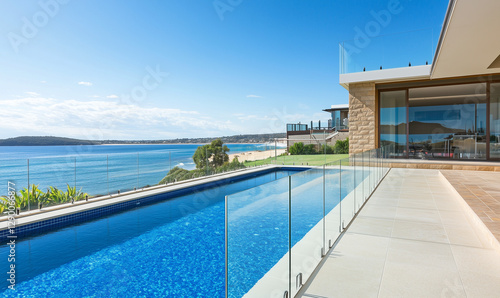 Modern glass fence by the ocean complemented by a pool, embodying luxury coastal architectural style