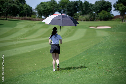 Golfer stands on a lush green golf course, holding a red and white umbrella relaxed yet attentive stance suggests she is either waiting for her turn to play or observing her shot.