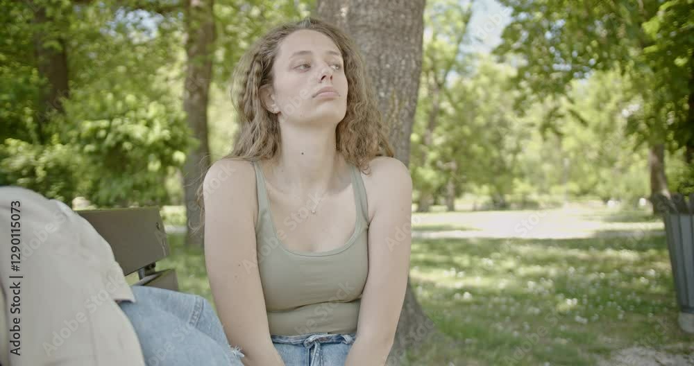A thoughtful young woman sits on a park bench, lost in contemplation on a sunny day. She reflects on life, enjoying the peaceful surroundings. A thoughtful young woman sits on a park bench, lost in contemplation on a sunny day. She reflects on life, enjoying the peaceful surroundings.