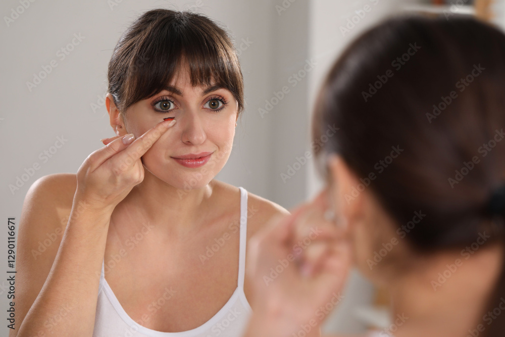 Young woman putting in red color contact lens near mirror indoors Young woman putting in red color contact lens near mirror indoors