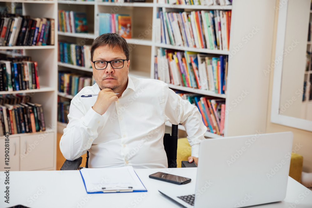 The guy sitting at the table with laptop on background of books The guy sitting at the table with laptop on background of books