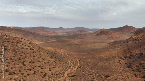 Aerial ascends from red, dry, arid, hilly desert landscape: cloud sky