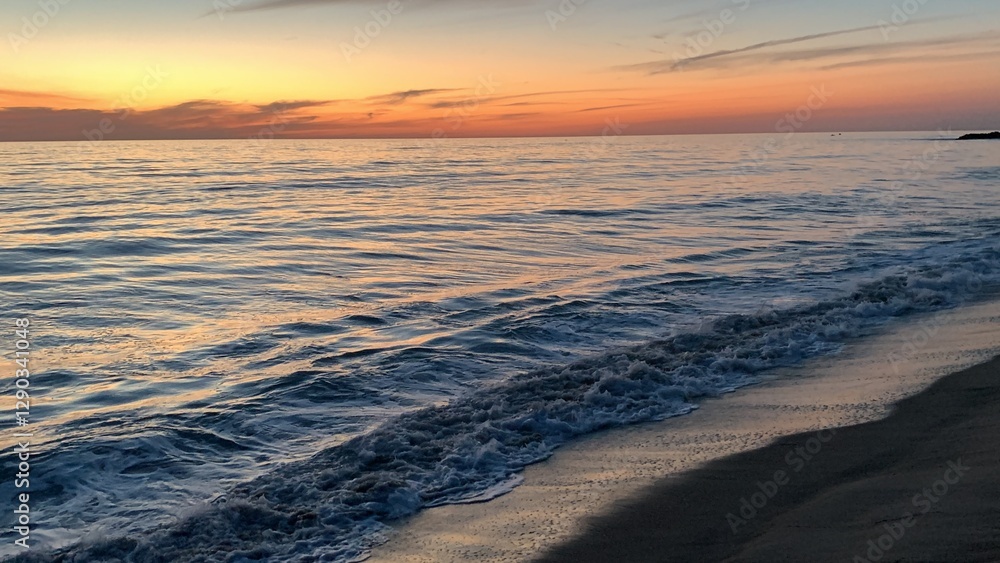 Obraz premium A color photo of calm ocean waters in Carlsbad, California, with gentle waves under a clear sky, bordered by a sandy beach.