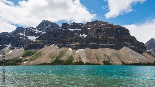 A refreshing view of imposing mountains set alongside a brilliant blue lake, showcasing the stunning contrast between the earthy tones and the sky's brilliance.