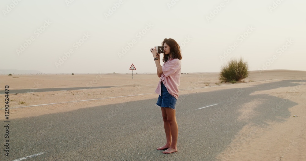 A young woman of European appearance shoots a video standing barefoot on a road covered with sand in the desert A young woman of European appearance shoots a video standing barefoot on a road covered with sand in the desert