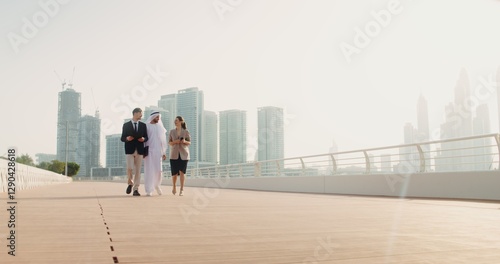 A man in traditional white Arab clothes with a laptop in his hands communicates with European business partners, walking down the street of a modern city