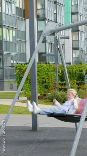 Two females in summer enjoying swing together at playground with sunny background and cheerful atmosphere