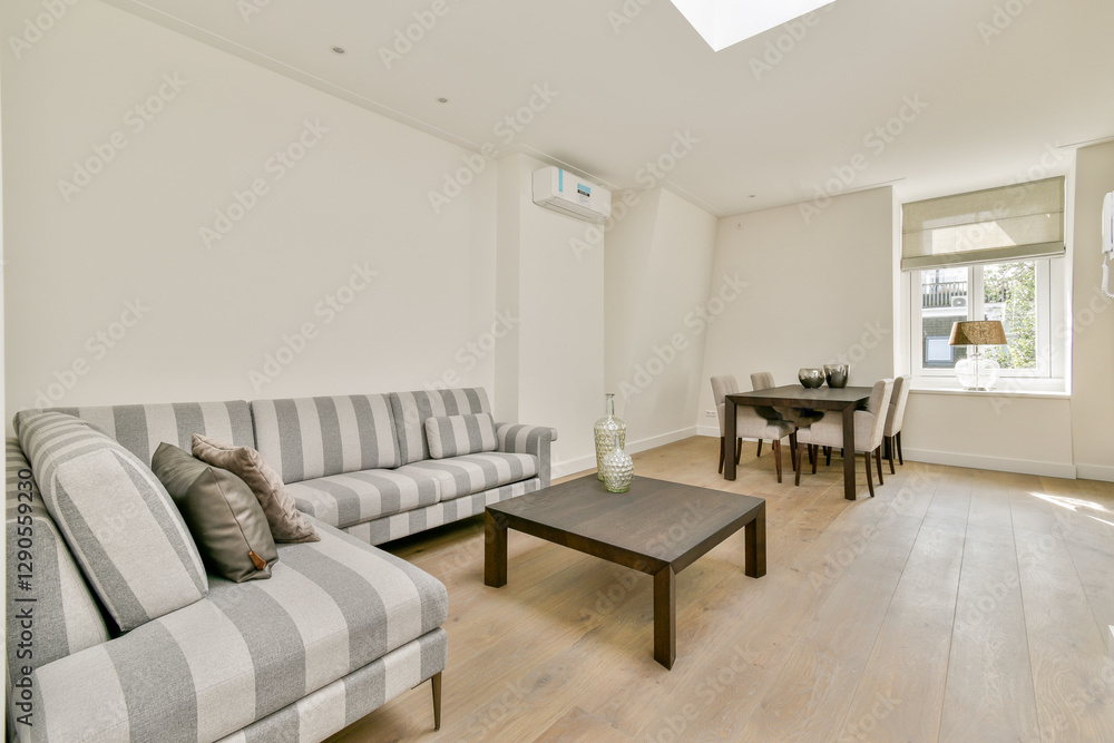 Fototapeta premium A stylish minimalistic living room featuring striped sofas and a wooden table. natural light filters through a large window, enhancing the serene atmosphere.