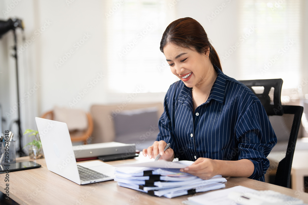Smiling Asian Businesswoman sitting and working hard with computer and lots of documents on the table in living room at home. Smiling Asian Businesswoman sitting and working hard with computer and lots of documents on the table in living room at home.