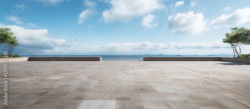 Fototapeta Naklejka Na Ścianę i Meble -  Empty beachfront park with vast empty stone floor, blue sky with clouds, calm sea in the background, flanked by green trees on either side.