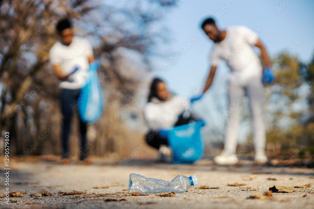 Obraz premium Selective focus on plastic bottle in nature with interracial volunteers collecting and recycling garbage in blurry background.