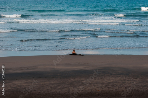 Surfer sitting on the sand watching the ocean waves at a remote beach photo