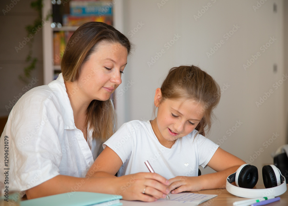 The parent helps the child. Happy family doing homework. Mother and daughter work on school assignments while sitting at the table. Children learning concept.