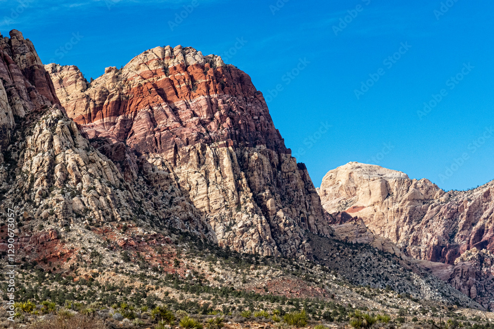 Obraz premium Striking image of colorful rock formations illuminated by bright sunlight, showcasing the beauty and diversity of nature in a clear blue sky backdrop.