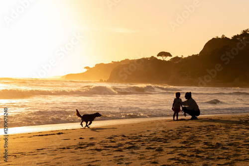 A heartwarming beach scene at sunset, where a parent and child share a moment by the waves while a dog joyfully runs along the shore.