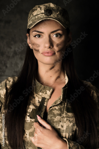 Portrait of a young woman in a military uniform and a cap with the coat of arms of Ukraine. The woman has camouflage on her face photo